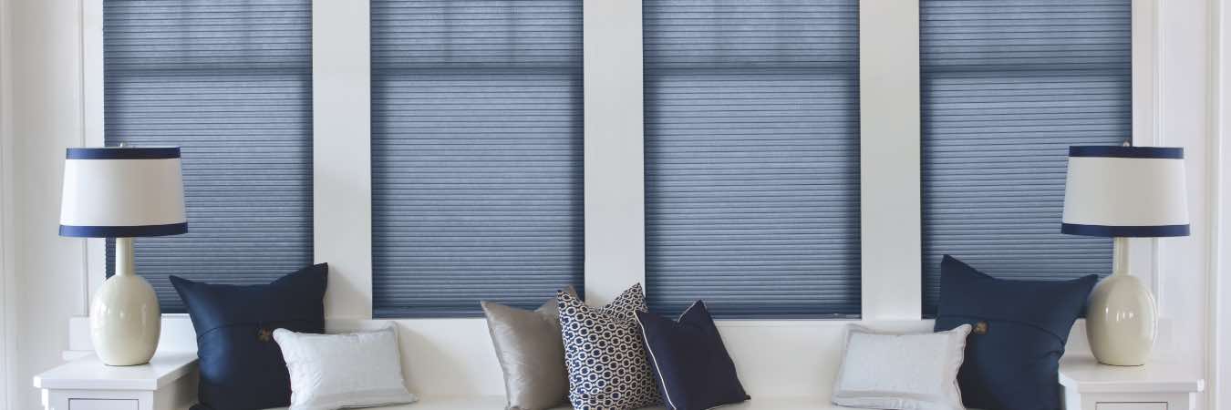 Blue cellular shades contrast against a white wall and white bench sitting area